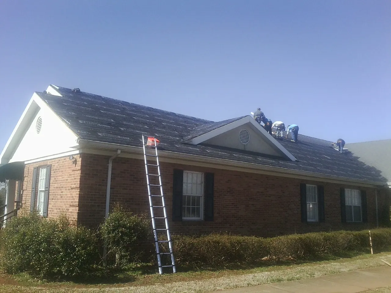 Crew tearing shingles off a brick ranch roof with a ladder set — Metal Roof Repair work by our crew in Yates City