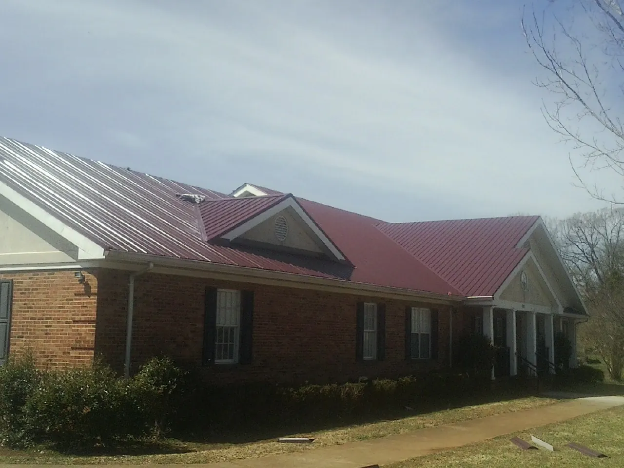 Red metal roof with gabled entries on a long brick building, from a Hail Damage Roof Repair job in Yates City