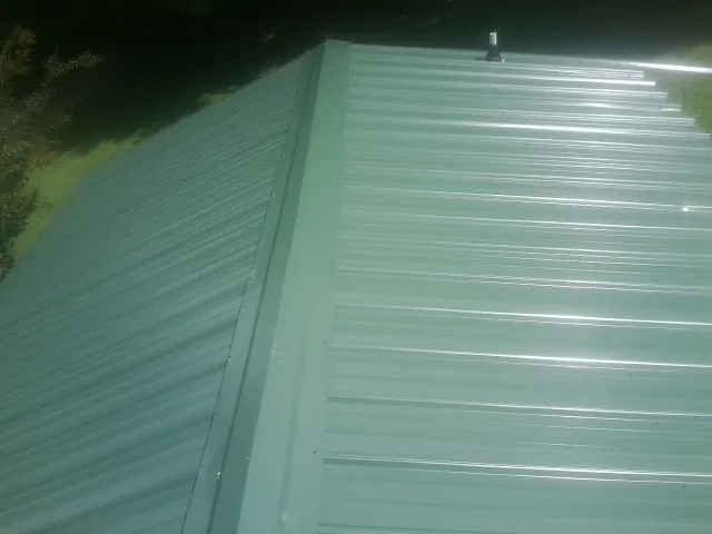 New green metal panels meeting at the ridge of a roof — Flat Roof Repair work by our crew in Yates City