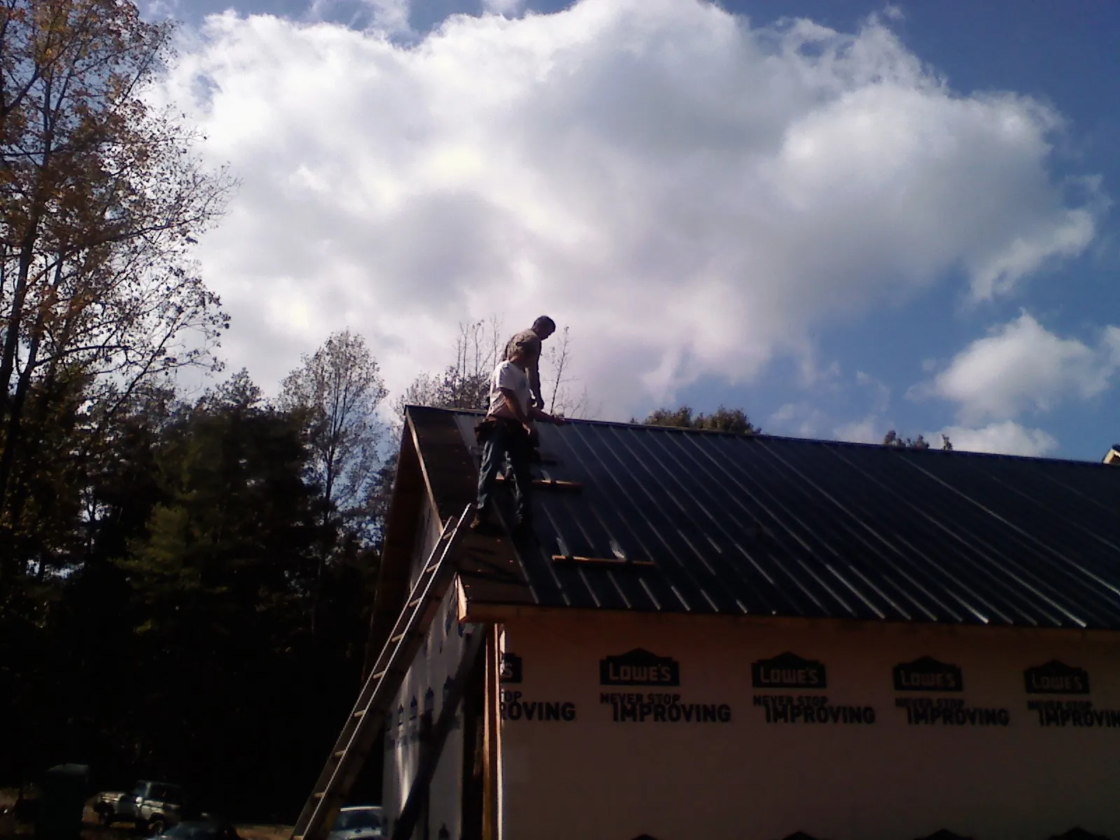 Roofer fastening dark metal panels high against a cloudy sky, from a Roof Inspection job in Yates City