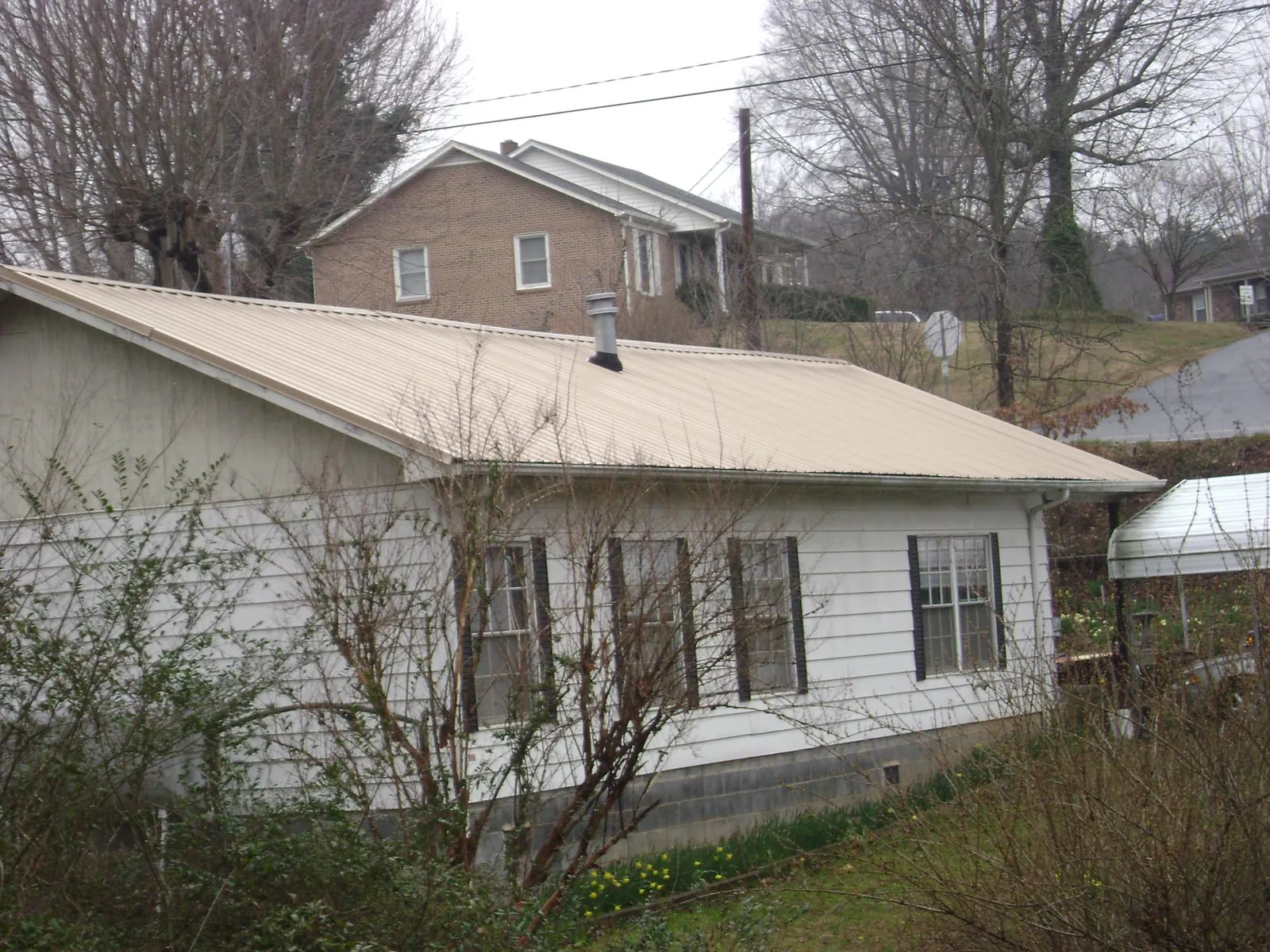 Tan metal roof on a white sided house set into a hillside — Commercial Roofing by Roofing Brothers in Yates City